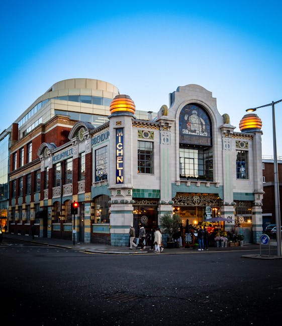 Exterior view of a historic sandstone building decorated with festive holiday lights, including illuminated star and gift box ornaments, alongside large caramel-colored panels. The building features arched windows with black frames, ornate stone detailing, and a prominent dome roof with decorative spires, situated in Knightsbridge. The scene is set during daytime under an overcast sky, with the decorations suggesting preparations for a seasonal event or celebration, highlighting a clean, well-maintained facade that reflects the importance of surface cleaning and preservation by Carpet Cleaning Knightsbridge for maintaining the building's appearance during festive times.